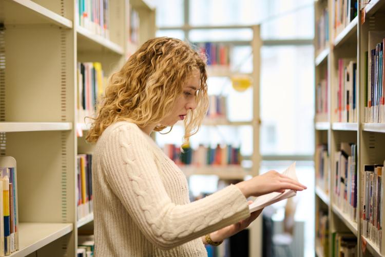 Zdjęcie kobiety przeglądającej książkę w bibliotece