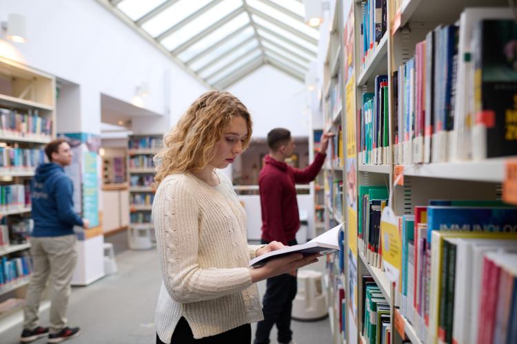 Studenci szukający książek w bibliotece