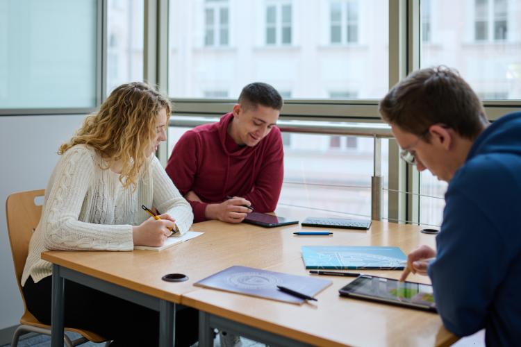 Na zdjęciu troje studentów siedzących przy stoliku w bibliotece