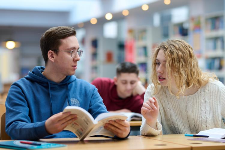 Na zdjęciu troje studentów siedzących przy stolikach w bibliotece