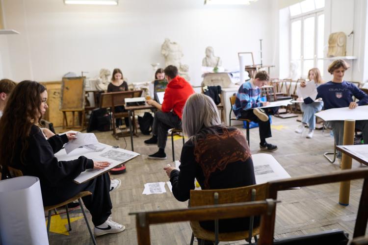 Na zdjęciu studenci architektury siedzący przy pulpitach i rysujący