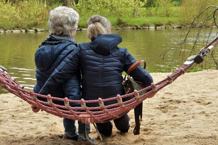 Na zdjęciu dwie starsze kobiety widziane od tyłu, siedzące na hamaku nad rzeką