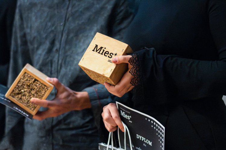 Na zdjęciu zbliżenie na dłonie trzymające kostkę z napisem Mies+