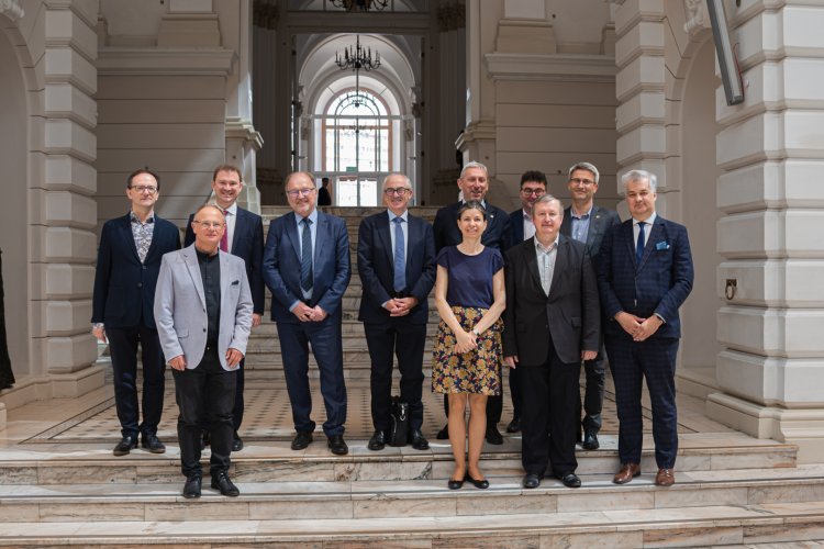 Na zdjęciu grupa osób na schodach w Dużej Auli Gmachu Głównego - przedstawiciele CERN-u i Politechniki Warszawskiej