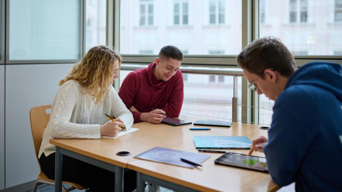 Na zdjęciu troje studentów siedzących przy stoliku w bibliotece