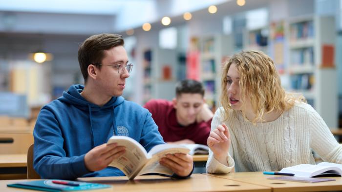 Na zdjęciu troje studentów siedzących przy stolikach w bibliotece