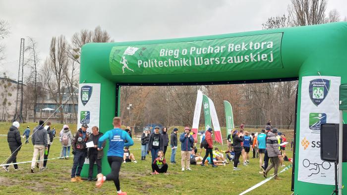 Na zdjęciu zawodnicy wbiegający na metę biegu z widocznym napisem Bieg o Puchar Rektora Politechniki Warszawskiej
