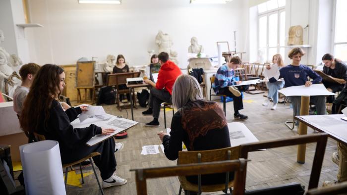 Na zdjęciu studenci architektury siedzący przy pulpitach i rysujący