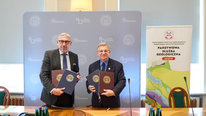 Za zdjęciu prof. Mariusz Malinowski oraz prof. Krzysztof Szmałek trzymający podpisane umowy, stojący na tle ścianki i roll-upu