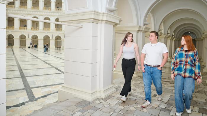 Na zdjęciu cztery osoby: dwie studentki i jeden student idą korytarzem w Gmachu Głównym PW