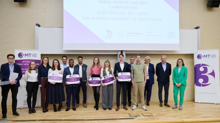 Zdjęcie przedstawia laureatów i jurorów konkursu Three Minute Thesis na Politechnice Warszawskiej stojących razem na scenie. Laureaci trzymają tablice z przyznanymi nagrodami.
