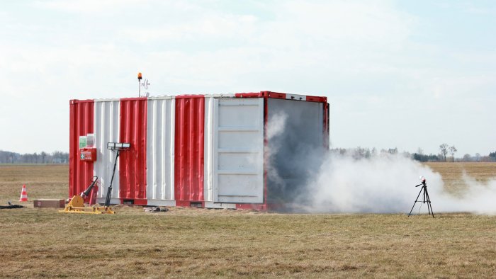 Na zdjęciu biało-czerwony hangar, z którego wydobywa się dym. Zdjęcie pokazuje testy silnika hybrydowego Aurora do rakiety Twardowsky 2