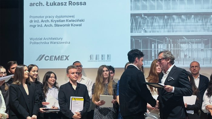 Na zdjęciu widać grupę ludzi. Na pierwszym planie arch. Łukasz Rossa odbierający nagrodę