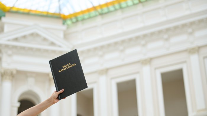 Na zdjęciu widać trzymaną pracę magisterską na tle wnętrza Gmachu Głównego PW