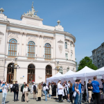 Zdjęcie Gmachu Głównego PW, ustawionych przed nim namiotów i zgromadzonych ludzi