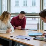 Na zdjęciu troje studentów siedzących przy stoliku w bibliotece