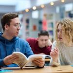 Na zdjęciu troje studentów siedzących przy stolikach w bibliotece