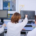 Na zdjęciu trzy osoby siedzące przy komputerze, jedna wskazuje ręką na ekran